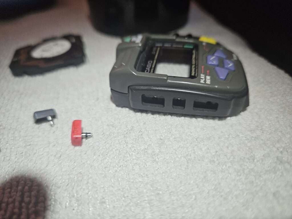 Close-up of Casio JG-100 empty button slots with loose side buttons next to the case.