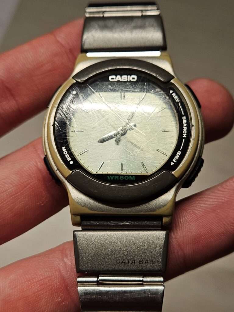 Casio ABX-53 Twincept watch held in hand showing scratched dial, steel bracelet with Data Bank clasp, WR50M, pre-restoration