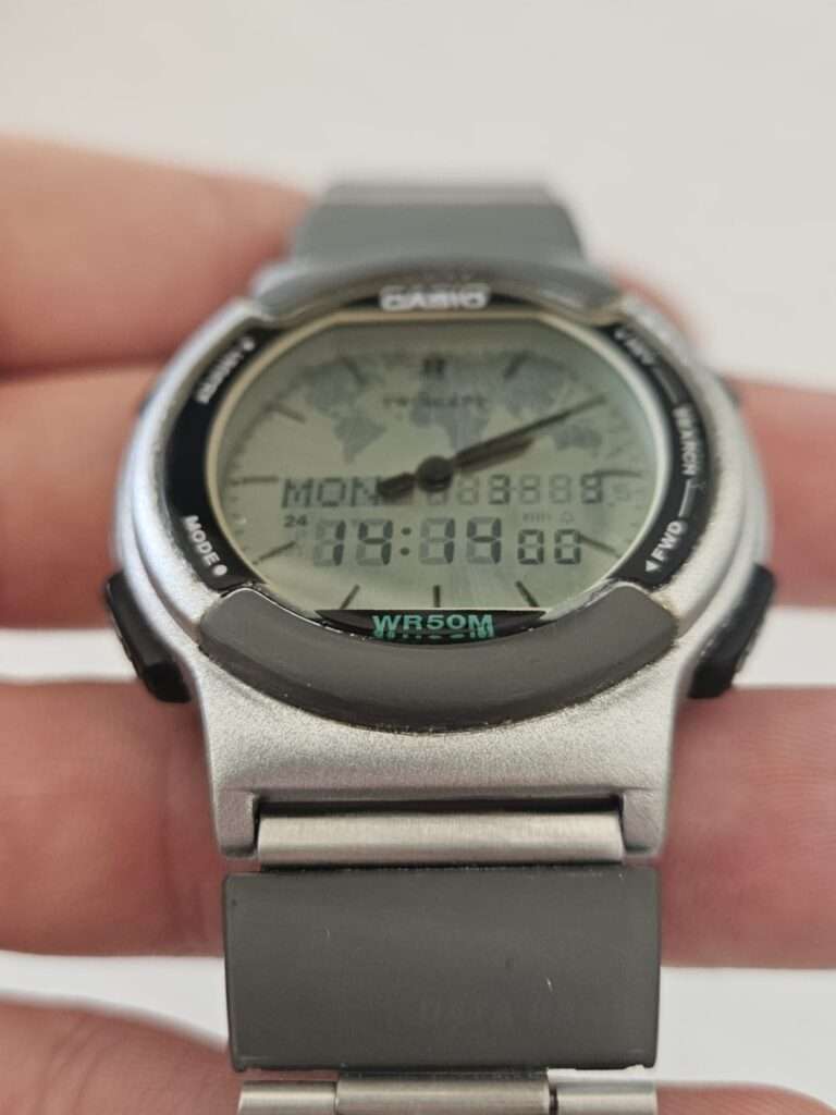 Casio ABX-53 Twincept held in hand showing world map dial overlay, analog hands, digital display MON 04:00, WR50M, post-restoration