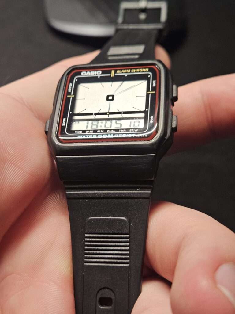 Restored Casio AE-11W Alarm Chrono held in hand showing clear LCD reading 16:80:57 and clean black case