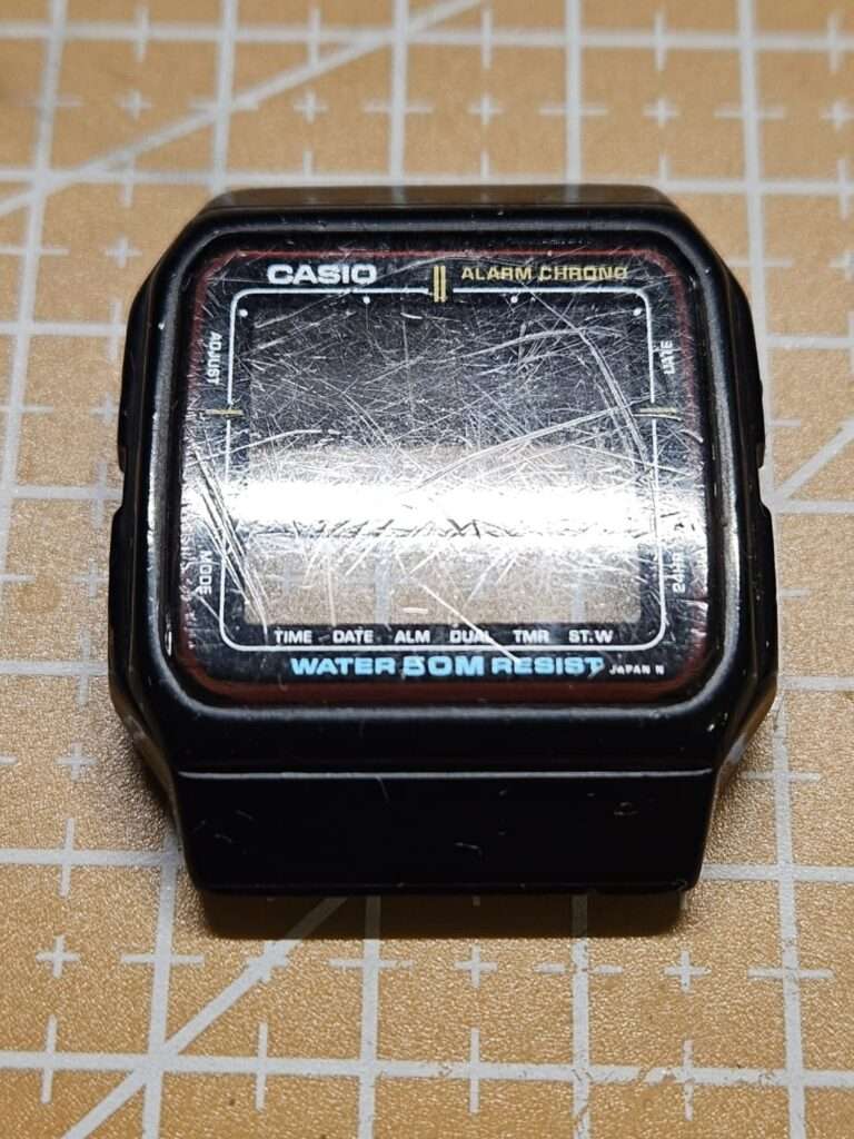 Casio AE-11W black resin watch case without strap showing deeply scratched crystal before restoration