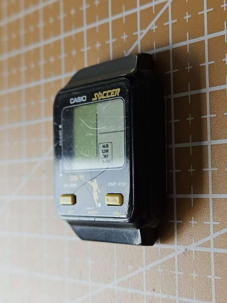 Casio GS-11 Soccer watch held in palm showing top-down view of worn LCD and gold buttons before restoration