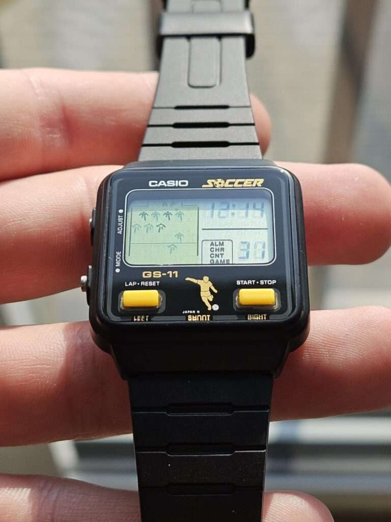 Casio GS-11 Soccer game watch after restoration flat lay on orange mat showing full strap and active LCD at 12:14