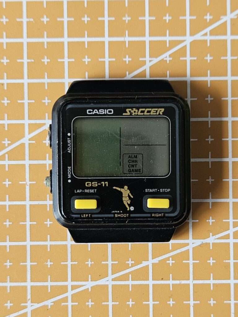 Casio GS-11 Soccer game watch three-quarter angle on orange mat showing LCD and case profile before restoration