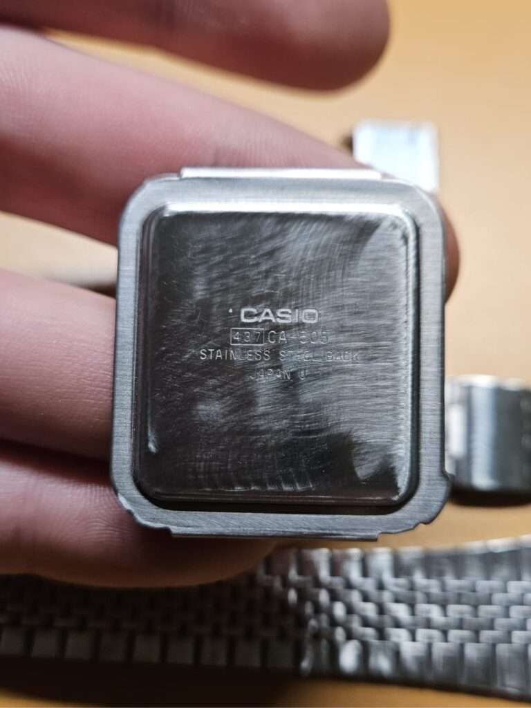 Casio CA-505 stainless steel back cover with deep scratches held in hand before sanding restoration