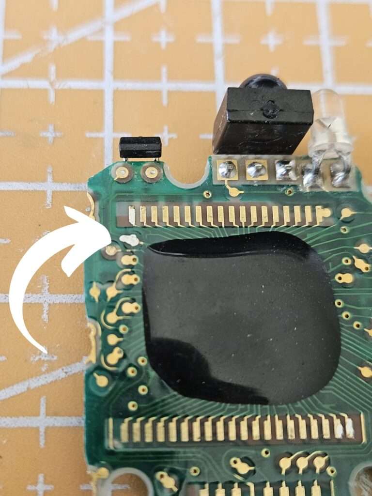 Casio JG-10 PCB board close-up showing repaired broken solder connection near IR emitter and LCD ribbon contacts during restoration
