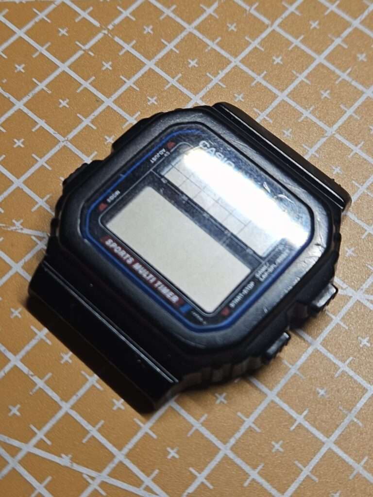 Casio STW-100 digital watch with dead LCD screen, angled view on cutting mat before repair