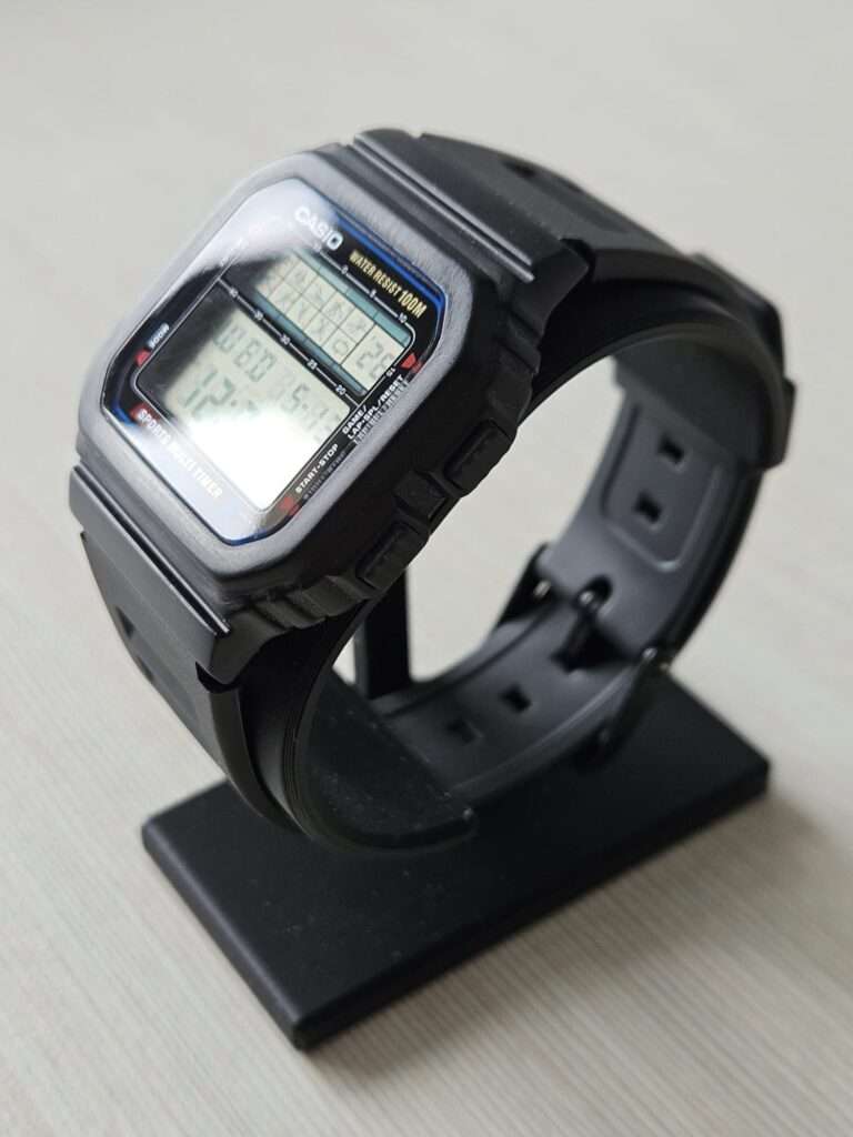 Casio STW-100 restored digital watch on black display stand, side view showing LCD and rubber strap