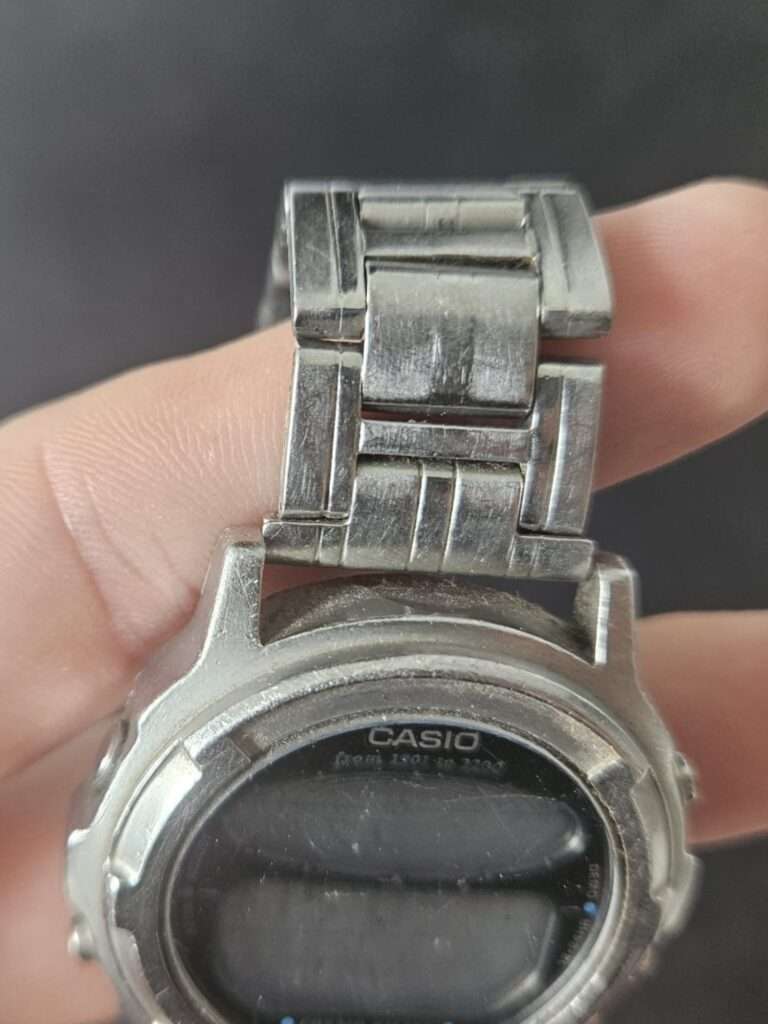 Casio CGW-500 Cosmo Phase stainless steel bracelet held in hand, showing deep scratches and wear before restoration