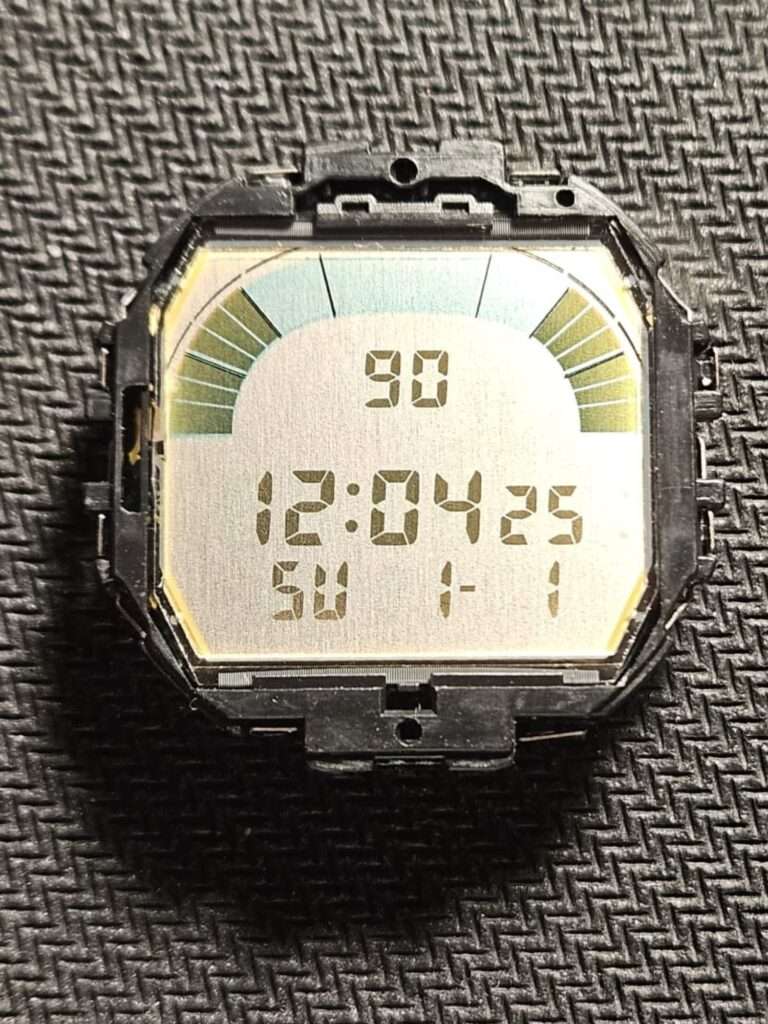 Casio W-95 LCD display module removed from case showing time 12:04 and Sunday on a green and blue scale