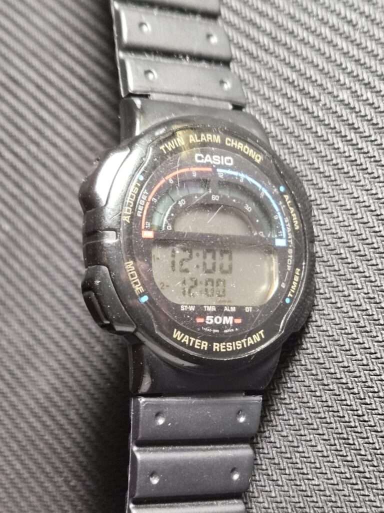 Casio W-95 Twin Alarm Chrono digital watch at an angle with black resin strap on a textured surface