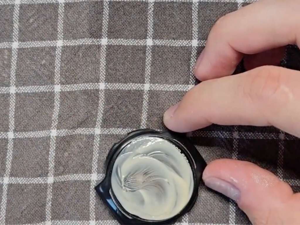 White polishing paste applied by hand to a black Casio watch crystal on a checkered cloth
