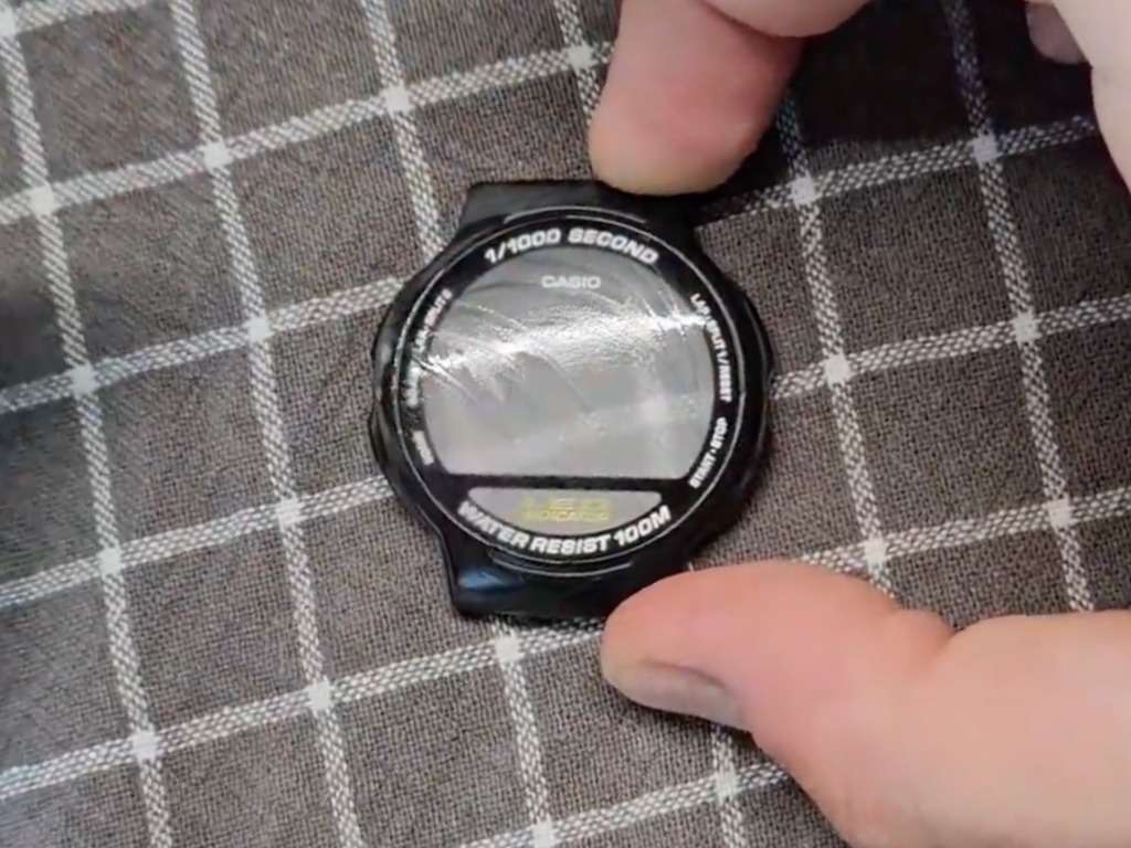Wet Casio watch crystal being hand-polished with visible swirl marks on the surface