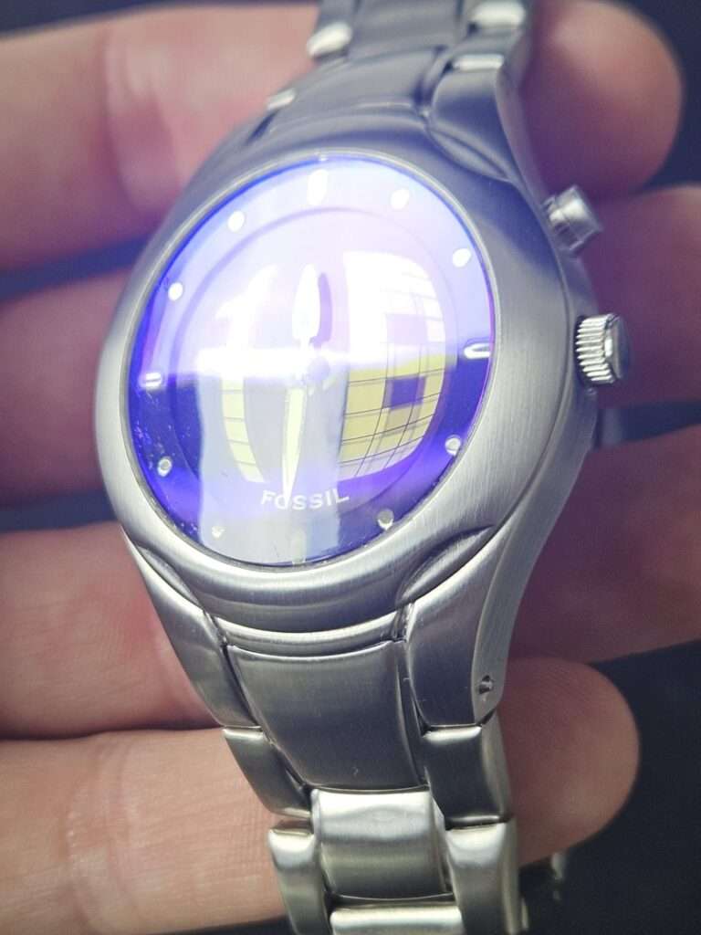 Fossil Big Tic JR8096 front view with polished crystal showing vivid purple and blue light reflection after restoration