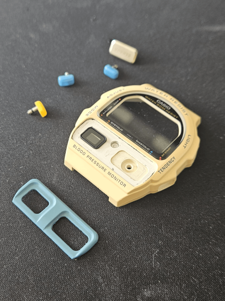 Disassembled Casio BP-100 case with buttons and strap loop removed for restoration