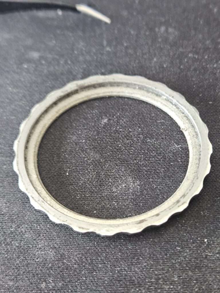 Dirty stainless steel fluted bezel ring from a Casio watch, removed and lying on dark fabric