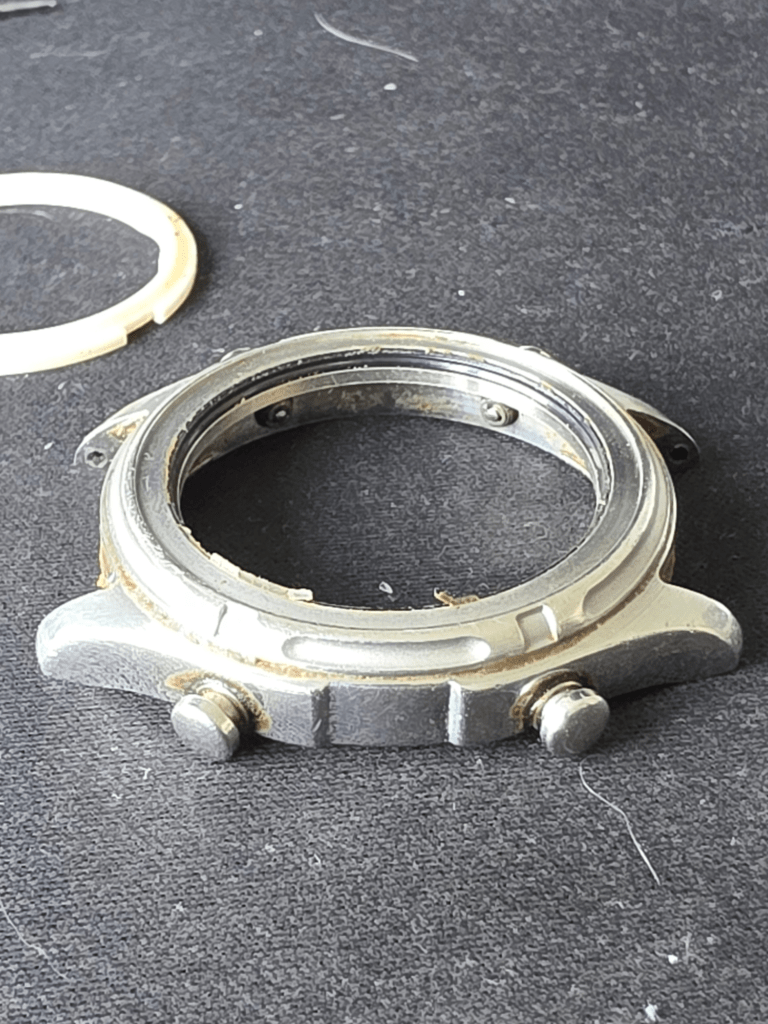 Disassembled Casio AW-600 watch case with corroded edges next to removed bezel ring